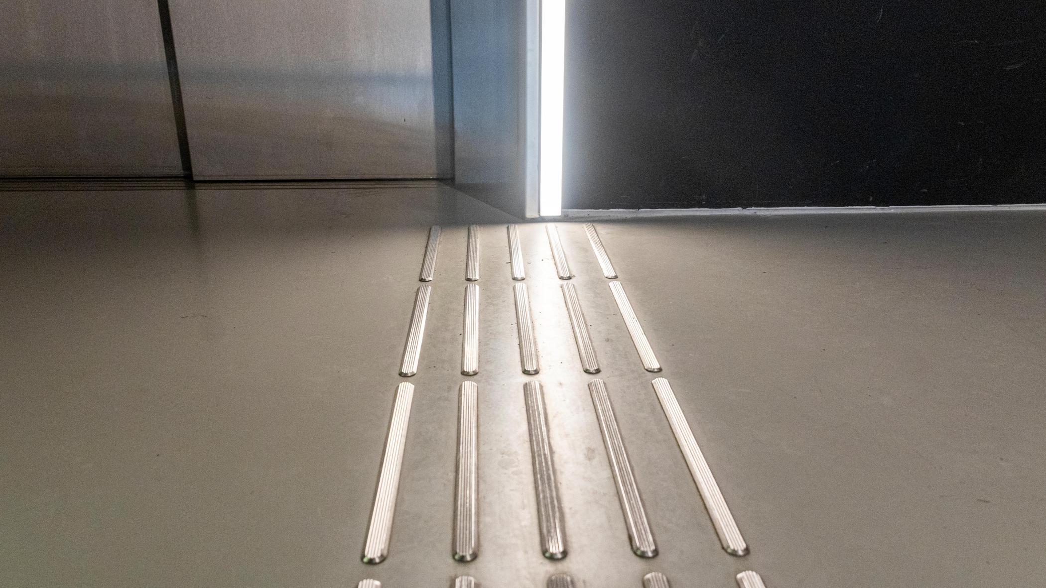 Taktile Bodenmarkierungen führen zu einem Durchgang, der teilweise geöffnet ist. Die Markierungen unterstützen die Barrierefreiheit.