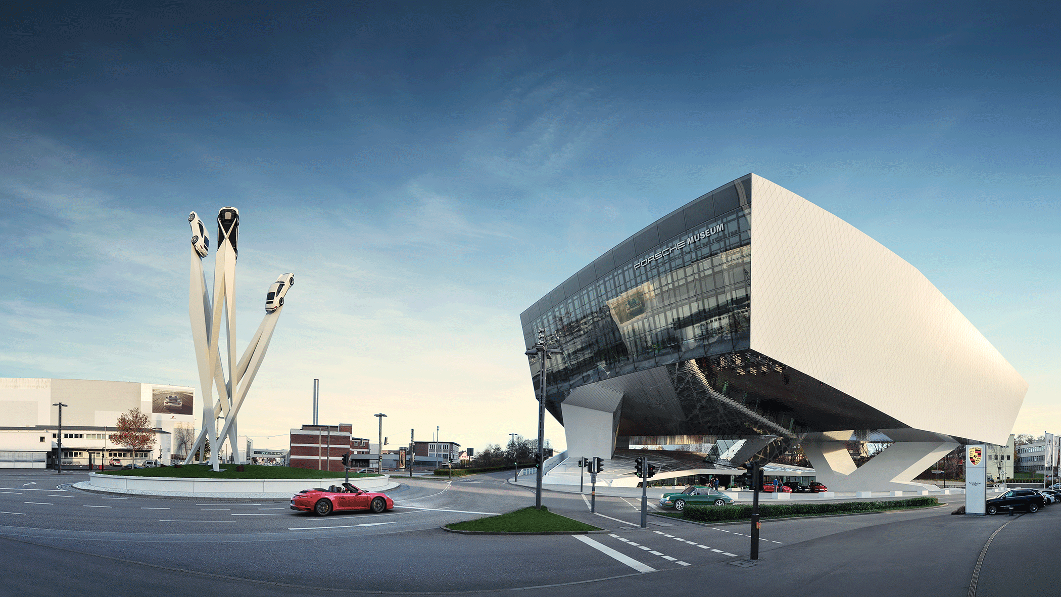 Das Porsche Museum in Stuttgart mit futuristischer Architektur und einer Skulptur von drei Autos auf hohen Säulen vor blauem Himmel.
