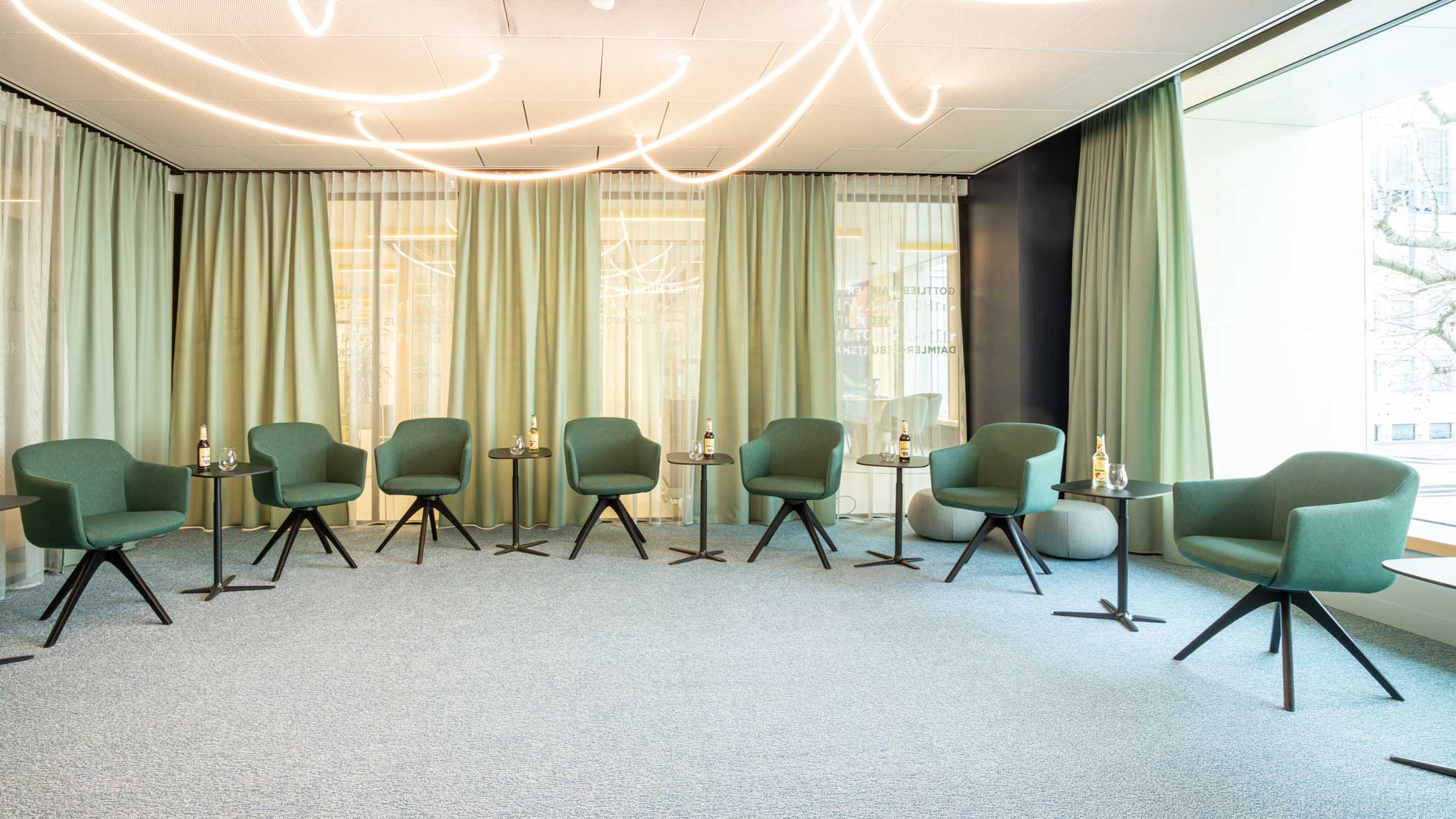 Grüne Stühle in einem Halbkreis mit je einem eingedeckten Beistelltisch.