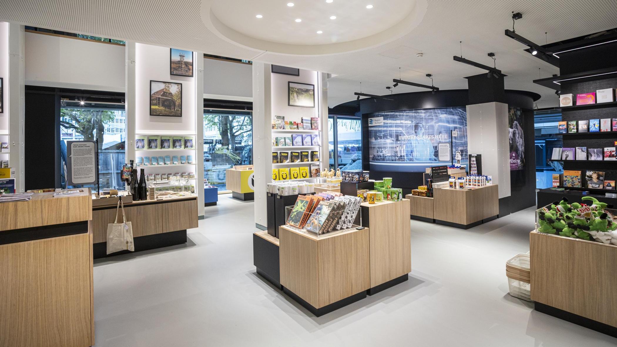i-Punkt Verkaufsraum, Stuttgart-Marketing GmbH, Sarah Schmid Helle, moderne Tourist-Information Stuttgart mit Regalen und Tischen, auf denen Souvenirs, Bücher und regionale Produkte präsentiert werden.