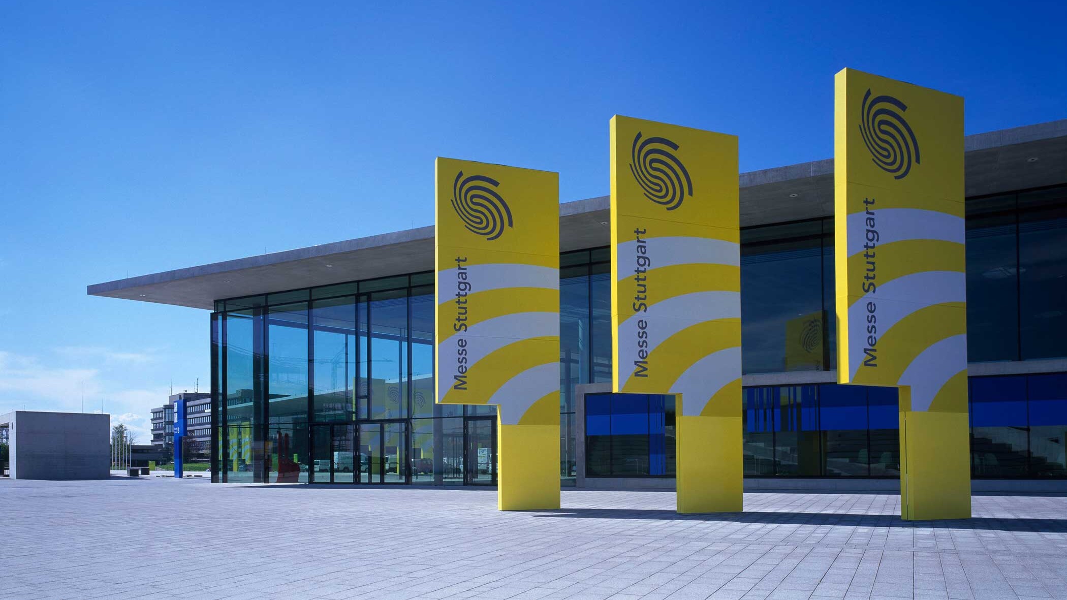 Messehalle, im Vordergrund drei gelbe Fahnen.